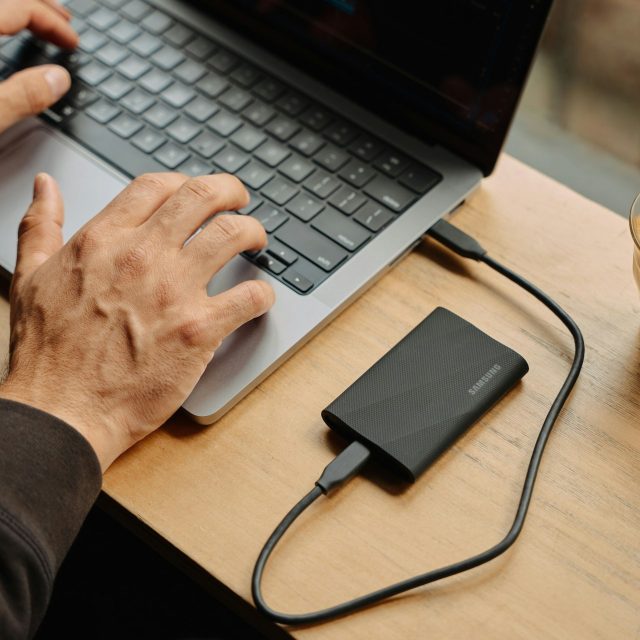 person sitting at a table using laptop with external hard drive